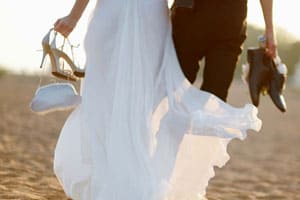 Mariés sur la plage avec chaussures dans la main