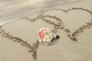 Deux coeurs dessinés sur le sable avec bouquet de la mariée posée au milieu